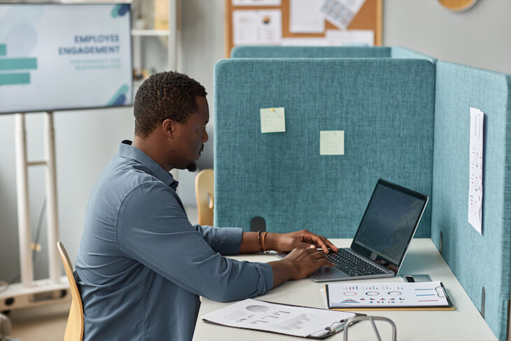 man works on laptop in cubicle