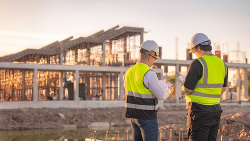 two engineers in hard hats and safety vests reviewing documents at construction site
