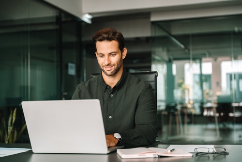 smiling professional man working on laptop at modern office desk